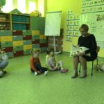 biblioterka w maseczce ochronnej czyta dzieciom w przedszkolu książkę