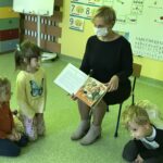 biblioterka w maseczce ochronnej czyta dzieciom w przedszkolu książkę