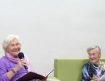 Teresa Lipowska i Anna Saciuk-Nowak siedzą na kanapie uśmiechnięte; pani Lipowska trzyma mikrofon