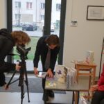 zdjęcie przedstawia młodzież ustawiającą statyw i kamerę, żeby sfilmować autorkę Agnieszkę Kazałę udzielającą wywiadu