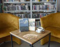 stolik i dwa fotele, na stoliku filiżanka kawy, ciastka i książki omawiane podczas spotkania