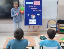 Pani bibliotekarka prezentuje uczniom plansze, na której znajduje się informacja o temacie warsztatów oraz pokazuje prototyp pracy plastycznej, którą uczniowie wykonają tj. żabkę.