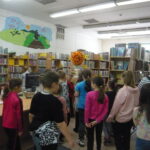 dzieci w trakcie zajęć stoją między regałami w bibliotece
