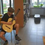 chłopak gra w bibliotece na gitarze