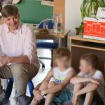prowadzący warsztaty Sławomir Brzózek rozmawia z dziećmi o energii; siedzą; obok na biurku dzbanek z wodą i ciastka, a także pojemnik na zużyte baterie