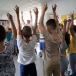 grupa dzieci stoi z wysoko uniesionymi rękami, wykonują ćwiczenia ruchowe