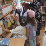 dzieci z przedszkola oglądają ksiażki na półkach bibliotecznych