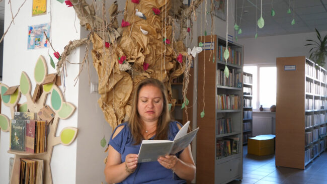 bibliotekarka czyta wiersz Romantyczność na tle papierowego drzewa w bibliotece