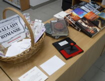 wiklinowy koszyk, a w nim zakładki do książek i logotyp wydarzenia; obok pamiątkowe pieczątki i książki - nagrody w quizie