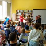 dzieci uczestniczą w spotkaniu autorskim; kierowniczka biblioteki wręcza kwiaty zaproszonym gościom - pisarce i lektorce