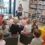 dzieci biorą udział w spotkaniu w biblitoece; słuchają pani bibliotekarki
