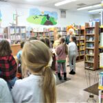 uczniowie szkoły podstawowej spacerują po bibliotece, poznając jej księgozbiór i zasady funkcjonowania
