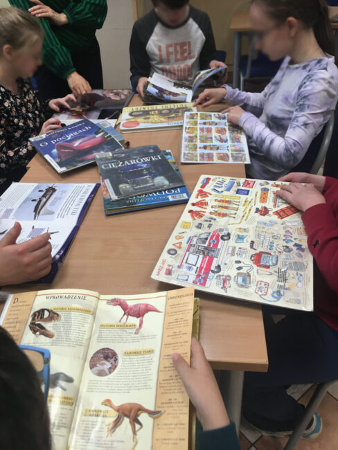 uczniowie przeglądają biblioteczne książki