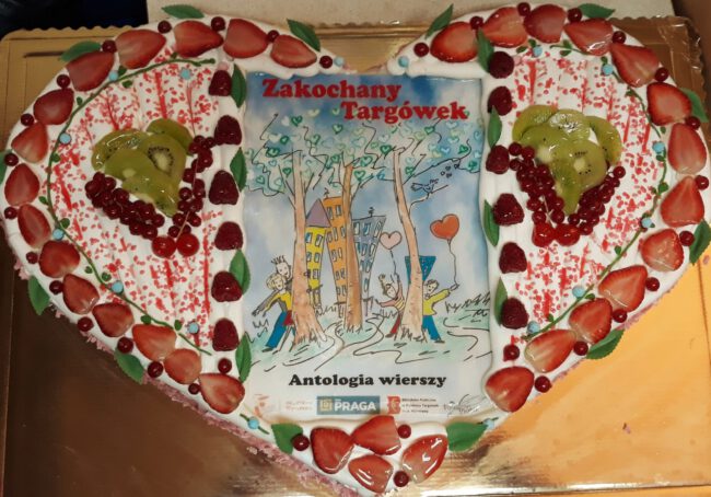 książka pt. Zakochany Targówek w środku tortu w kształcie serca, ozdobionego truskawkami i kiwi