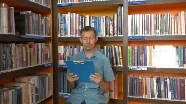 bibliotekarz czyta fragment Kariery Nikodema Dyzmy; w tle regał wypełniony książkami