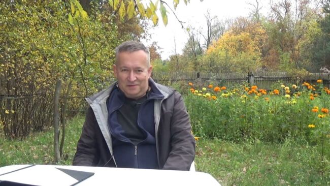 Krzysztof Gajda siedzi przy stoliku w ukwieconym ogrodzie