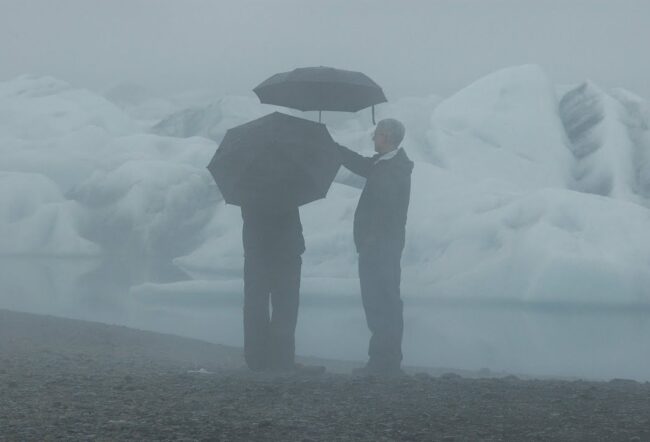 dwóch mężczyzn z parasolami stoi przy lodowcu na Islandii
