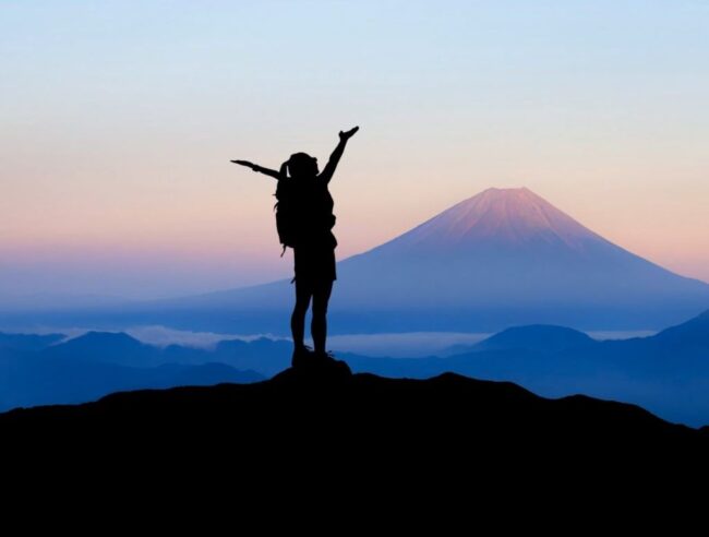 kobieta stoi o zmierzchu na szlaku górskim, wokół góry, na dalszym planie wulkan Fuji