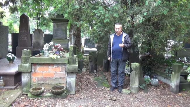 Krzysztof Gajda stoi przy jednym z cmentarnych grobów