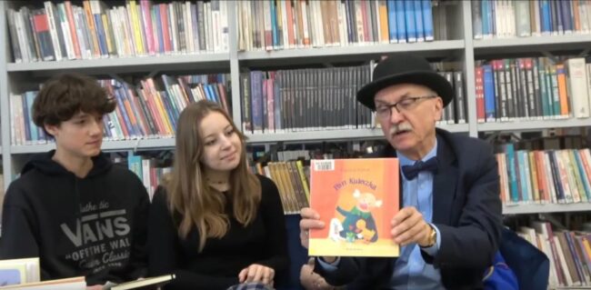 Wojciech Widłak prezentuje swoją książkę, obok niego na sofie siedzą licealiści; pisarz udziela im wywiadu