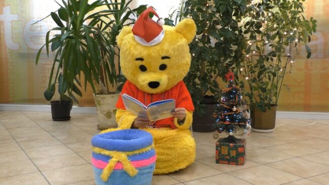 maskotka biblioteki - miś - siedzi na podłodze i czyta książkę