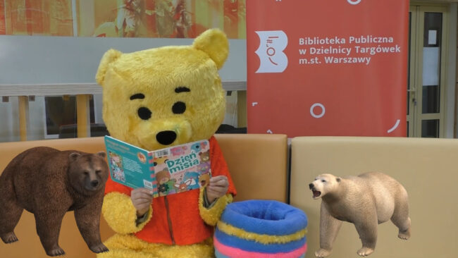 maskotka biblioteki - miś - czyta książkę Dzień misia, obok niego grafika - niedźwiedź polarny i niedźwiedź brunatny