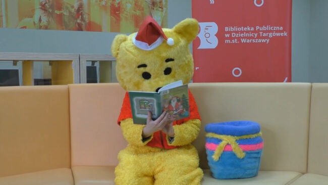 maskotka biblioteki - miś czyta książkę w czapce mikołaja