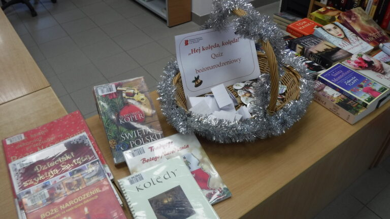 koszyczek ozdobiony łańcuchem choinkowym, w koszyczku przypinki okolicznościowe, dookoła na biurku książki o tematyce świątecznej