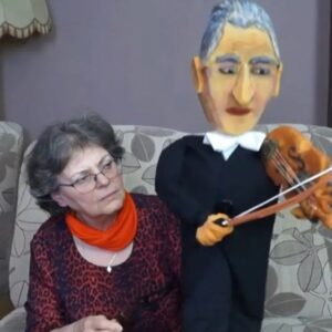 kobieta siedzi na sofie, trzyma dużą lalkę - mężczyznę grającego na skrzypcach