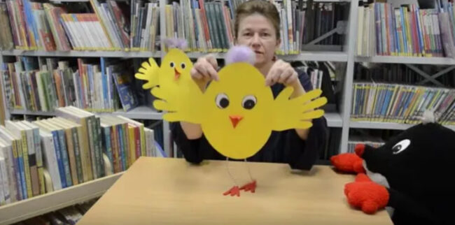 bibliotekarka pokazuje papierową ozdobę - wielkanocnego kurczaka.