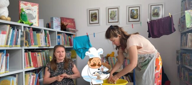 bibliotekarki recytują wiersze, jedna z nich również pierze ubrania w misce z wodą, pośrodku animacja - postać kucharza