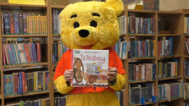 maskotka biblioteki trzyma książkę Doroty Gellner pt. Wścibscy