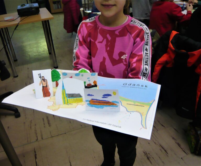 dziewczynka pokazuje pracę plastyczną - makietę papierową z atrakcjami Polski