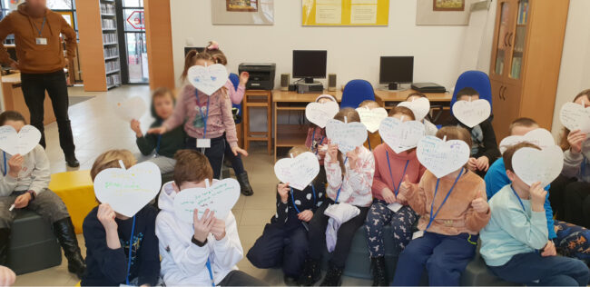 dzieci pokazują swoje papierowe serca walentynkowe z miłymi słowami napisanymi przez koleżanki i kolegów