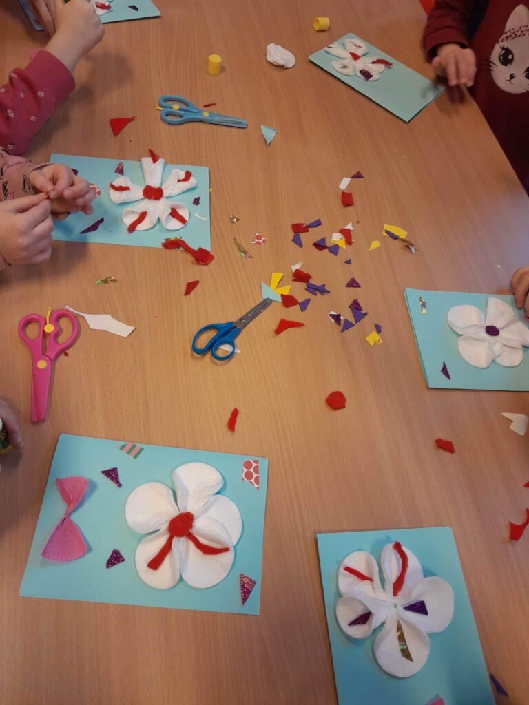 prace plastyczne dzieci - papierowe kwiaty - leżą na stolikach, obok nich nożyczki