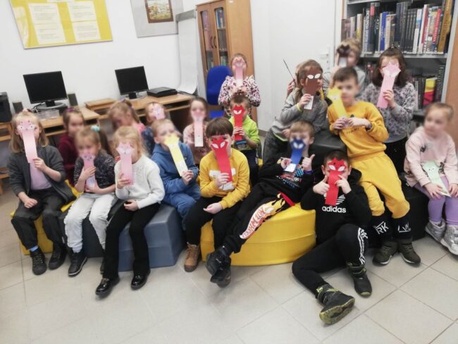 dzieci biorące udział w zajęciach bibliotecznych prezentują swoje prace plastyczne