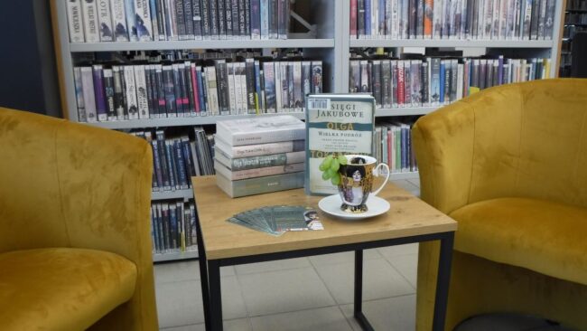 książki Olgi Tokarczuk na stoliku w bibliotece; obok nich filiżanka na spodku