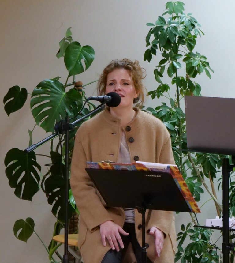 wokalistka duetu Pełnia śpiewa na scenie czytelni; w tle dużo zieleni kwiatów doniczkowych