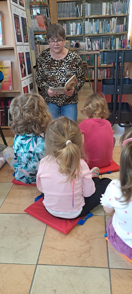 dzieci słuchają książki czytanej przez bibliotekarkę