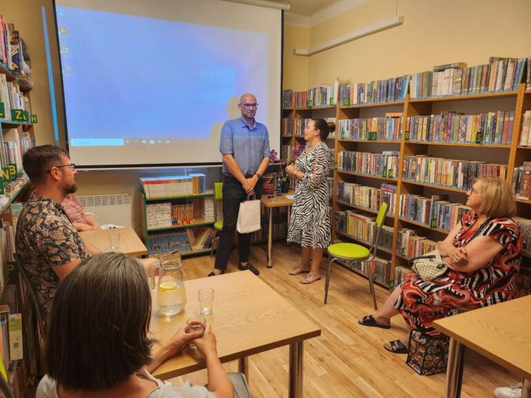Autor Maciej Zajaczkowski i moderujaca rozmowę pani bibliotekarka, stoją na tle ekranu, na którym prezentowane były zdjęcia z podróży autora.