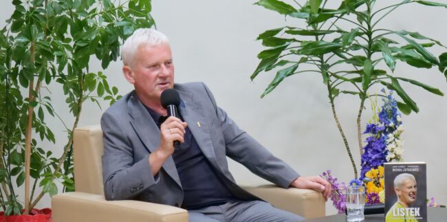 Pan Michał Listkiewicz siedzi przy stole. Na stole m.in. książka "Listek - Najciekawiej jest po końcowym gwizdku".