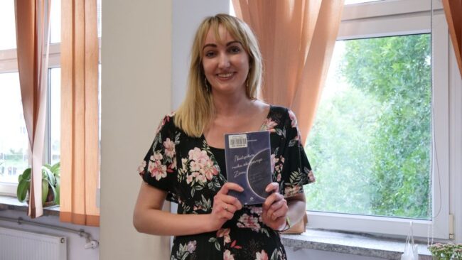 poetka w wieku ok. 30 lat pozuje do zdjęcia, trzymając swój tomik poezji