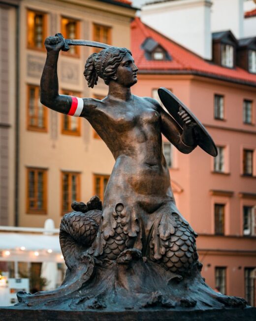pomnik syrenki warszawskiej z biało-czerwoną opaską na ręce trzymającej miecz
