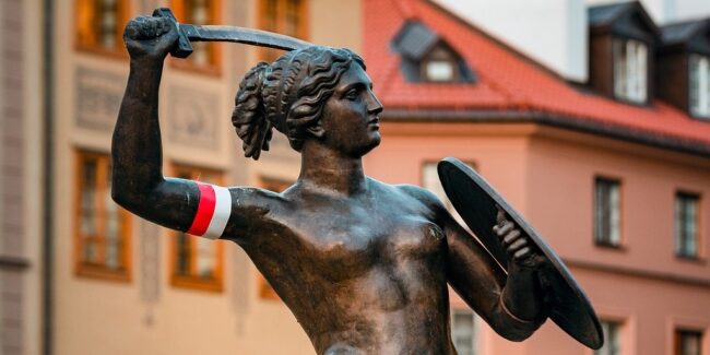 pomnik syrenki warszawskiej z biało-czerwoną opaską na ręce trzymającej miecz