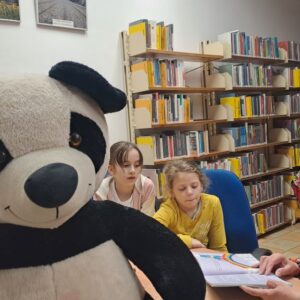 duża maskotka pandy, dzieci słuchają książek czytanych przez wolontariuszkę