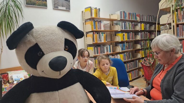 duża maskotka pandy, dzieci słuchają książek czytanych przez wolontariuszkę