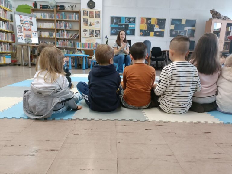grupa dzieci siedzi na macie w bibliotece