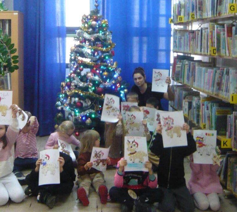 dzieci pozują do zdjęcia przy choince w bibliotece, trzymają swoje prace plastyczne