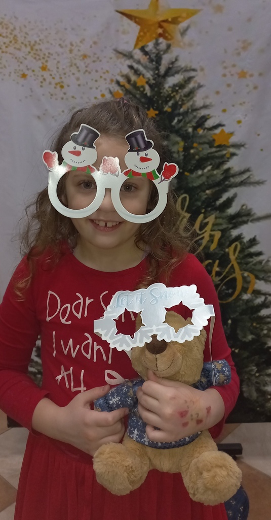 dziewczynka pozuje do zdjęcia na tle choinki, ma okulary w kształcie bałwanków