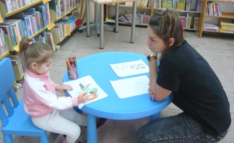 dziewczynka i bibliotekarka siedzą przy stoliku do prac plastycznych